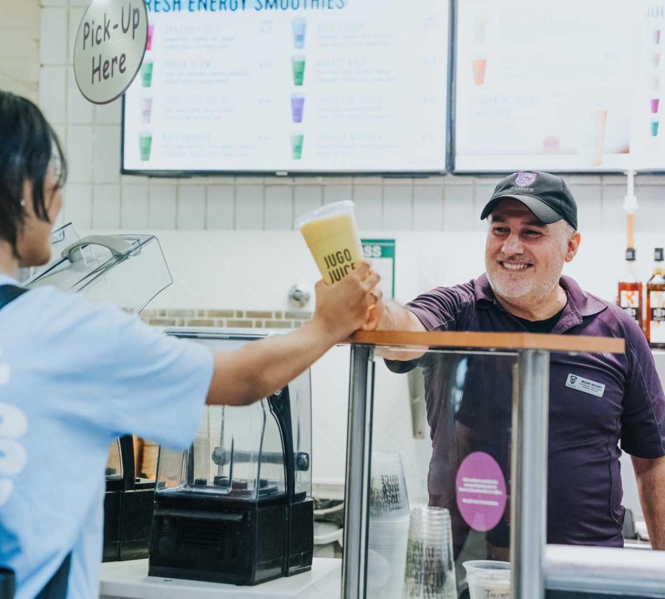 A staff member serving a student a Jugo Juice smoothie